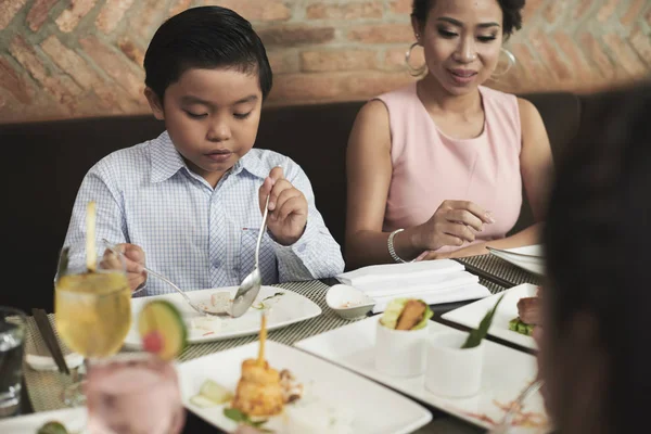 アジアの男の子がテーブルに座って レストランで近くの母親と昼食を食べます — ストック写真