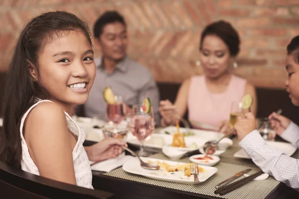 在餐厅吃饭时 漂亮的微笑女孩和家人坐在桌旁的肖像 — 图库照片