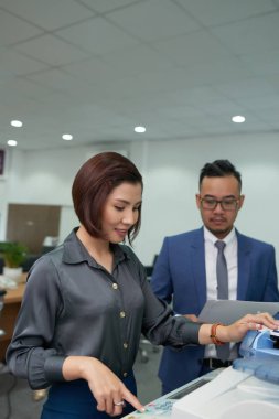 Genç işkadını onun tarafından yakın ayakta onun meslektaşı ile fotokopi makinesinde belgenin kopyasını yapma ve ofiste onun dönüş bekliyor
