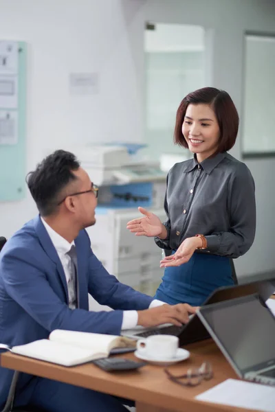 Lächelnde Asiatische Geschäftsfrau Gespräch Mit Geschäftsmann Während Seinem Arbeitsplatz Sitzt — Stockfoto