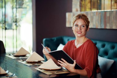 Açık menü ile kafe masada oturan ve garson bekliyor parlak kırmızı bluz güzel sarışın kadın