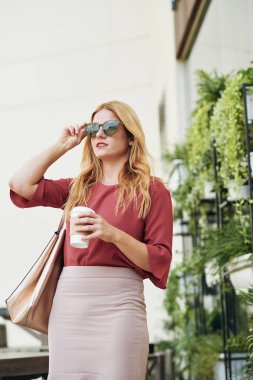 Sokakta duran ve güneş gözlüğü takan kahve fincanı ile genç kendine güvenen iş bayan Portresi