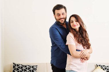 Mutlu gülümseyen sakallı Hintli adamın güzel kız arkadaşına arkadan sarılarak kameraya bakabakmış portresi