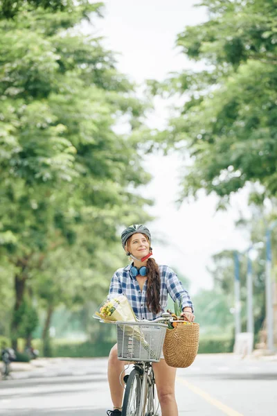微笑快乐的年轻女子与花束和购物篮杂货骑在城市公园 — 图库照片