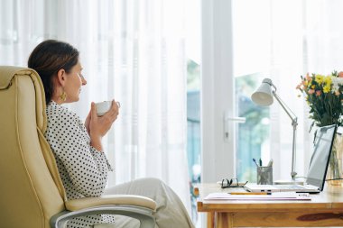 İş kadını gözlerini kapatıyor ve elinde porselen bardakta sabah kahvesinin lezzetli aromasını kokluyor