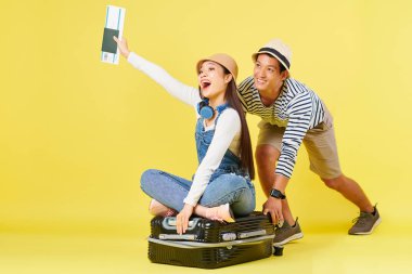 Panama şapkalı mutlu genç Asyalı adam üzerinde bilet oturan oldukça bağıran kadın ile bavul iterek