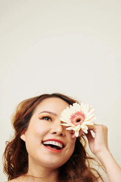 彼女の顔の前にガーベラの花を保持し 白い背景に孤立した笑顔を持つ巻き毛を持つ幸せな若いアジアの女性 — ストック写真