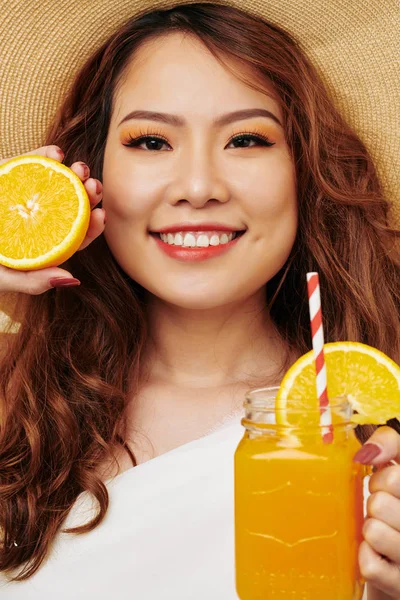 肖像亚洲美丽的女人与红色长卷发微笑在相机 而拿着玻璃橙汁 — 图库照片