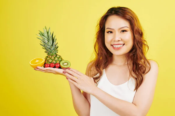亚洲红头发妇女的肖像在镜头前微笑 手里拿着各种热带水果 孤立在黄色背景上 — 图库照片