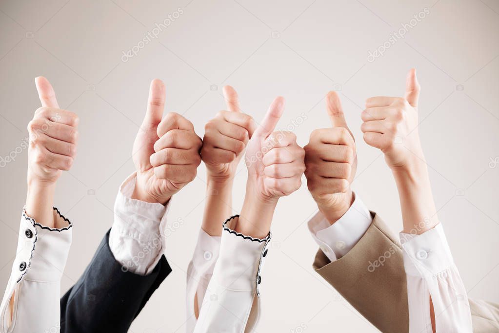 Close-up of group of business people raising their arms up and showing thumbs up isolated on white background