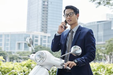 Yakışıklı genç Vietnamlı girişimci scooter yanında duran ve telefonla arama 