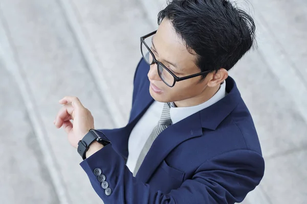彼のスマートウォッチ上の通知をチェックメガネで若いアジアの起業家は 上から見て — ストック写真