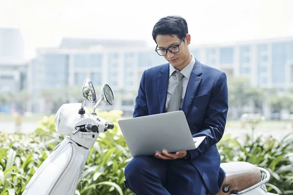 Pozytywny Młody Wietnamski Biznesmen Siedzi Skuterze Odpowiadając Maile Swoim Laptopie — Zdjęcie stockowe