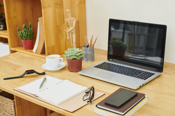 Image of wooden table with laptop computer notepad and other office supplies at modern office
