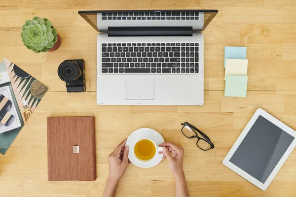 坐在木桌旁喝茶的妇女的特写镜头 在办公室使用笔记本电脑和平板电脑时 — 图库照片