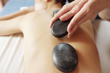 Profesyonel masör elleri spa salonu genç kadın müşteri omurga boyunca sıcak bazalt taşlar koyarak