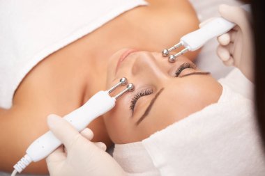 Kozmetolojist tarafından yüz yapımı için gençleştirme işlemi sırasında gözleri kapalı rahatlatıcı genç güzel kadının yakın çekim