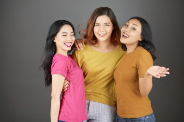 Birbirini kucaklayan ve gri arka planda izole kameraya gülümseyen Asyalı mutlu arkadaş grubunun portresi