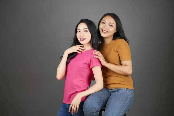 两个亚洲姐妹在灰色背景上一起微笑和在镜头前摆姿势的肖像 — 图库照片