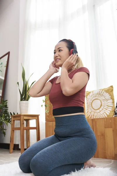 リビングルームの床に座って音楽を聴くヘッドフォンで若い肯定的なアジアの女性 — ストック写真