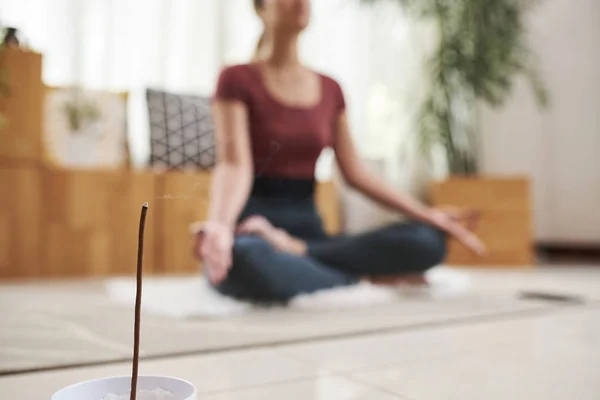 Burning aroma stick and woman meditating in lotus position in background