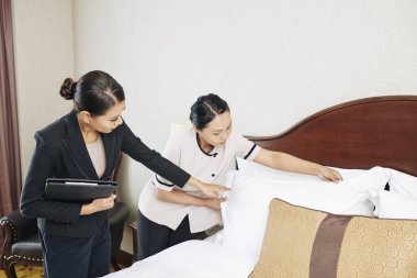 Otel odasında hizmetçi için yatak yapmak için nasıl gösteren formalwear Asyalı genç otel yöneticisi