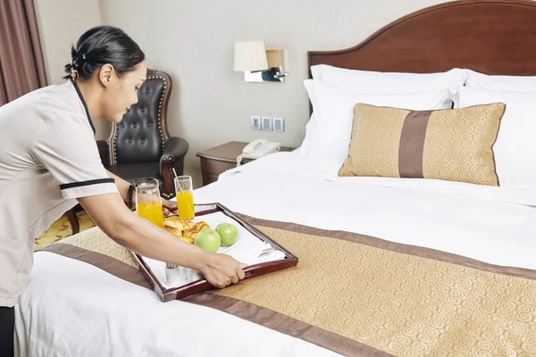 制服を着たアジアのメイドが食べ物や飲み物でトレイを持ってきて ホテルの部屋のベッドの上に置く — ストック写真