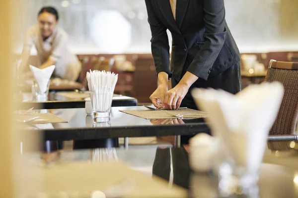 ウエイトレスがバックグラウンドで働くレストランでテーブルを置くマネージャーのクローズアップ — ストック写真