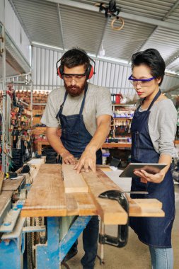 Profesyonel marangozluk işçisi nasıl workbench ahşap plakalar kesmek için genç kadın çırak gösteren