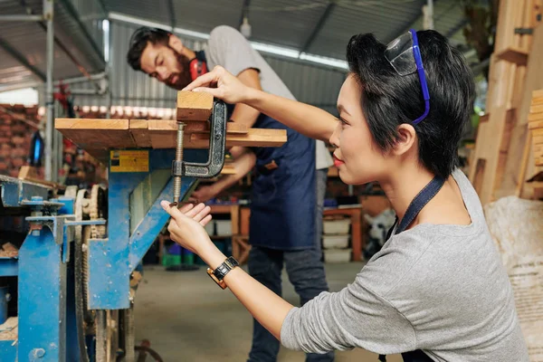 女性大工調整ワークベンチと彼女の同僚は バラバラにそれをカットするためにテーブルの上に木製の板を置きます — ストック写真