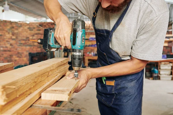 木製板に青いデニムエプロン掘削穴のプロの大工 — ストック写真