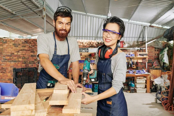 Happy multi-ethnic team of carpenters working with wood at furniture manufacture