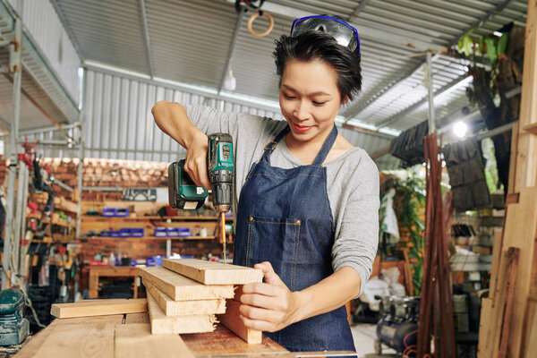 Smiling pretty carpenter using cordless electric screwdriver