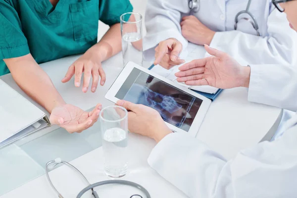 Group of doctors sitting at table and discussing jaw x-ray of patient, trying to define diagnosis and way of treatment