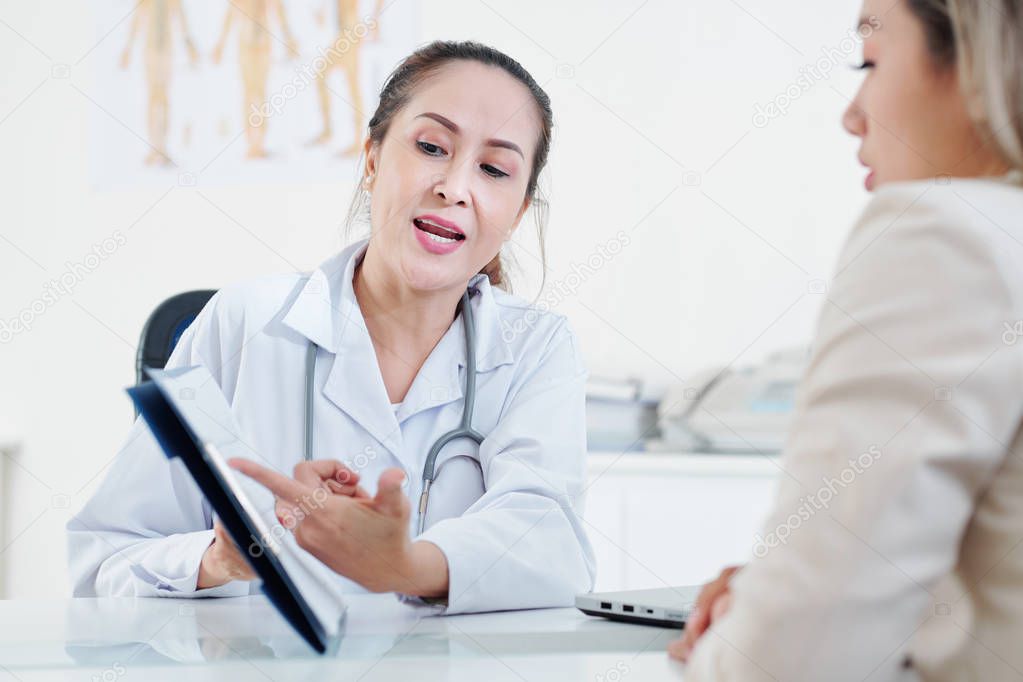 Serious mature experienced cardiologist explaining cardiogram to female patient