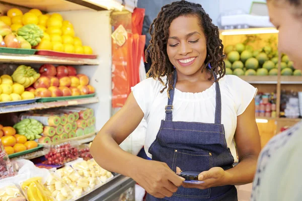 非洲女售货员在围裙里拿着手机 在超市用信用卡购物的特写 — 图库照片