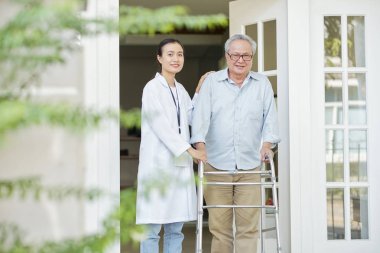O huzurevinde yaşayan Asyalı genç hemşire ile birlikte açık havada yürüyen walker ile Asyalı kıdemli adam Portresi
