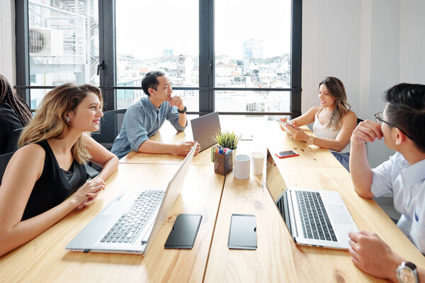 Деловые партнеры, сидящие на рабочем месте и работающие на ноутбуках и обсуждающие онлайн-работу во время рабочего процесса в офисе
