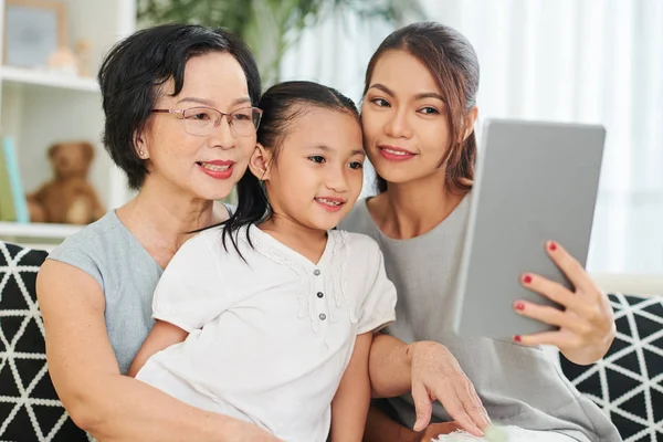 Happy Asian family generation sitting on sofa smiling and posing at camera of digital tablet at home