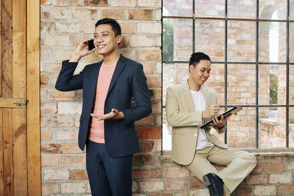 Cheerful Young Asian Entrepreneur Talking Phone His Cheerful Coworker Sitting — Stock Photo, Image