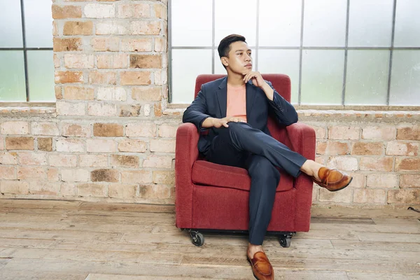 年轻自信的亚洲企业家穿着时尚西装坐在天鹅绒扶手椅上 思考新业务的想法 — 图库照片