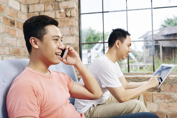 快乐笑年轻的亚洲启动者在电话中交谈时 他的同事使用数字平板电脑上的应用程序 — 图库照片