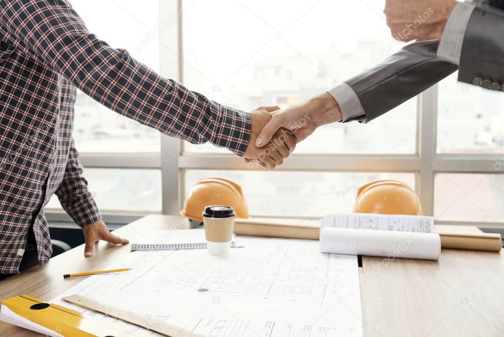 Close-up of businessman and architect standing and shaking hands to each other after successful discussion of new project at meeting at office