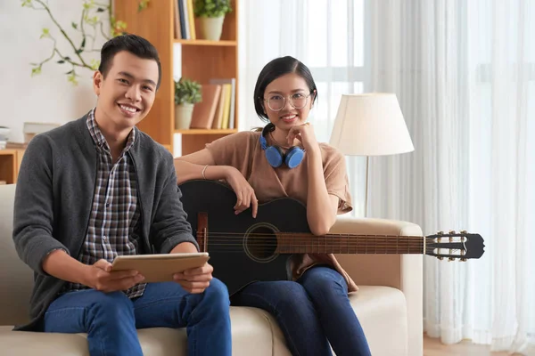 亚洲年轻夫妇坐在一张小瓦上 一边弹吉他 在家里写新歌 一边对着相机微笑 — 图库照片