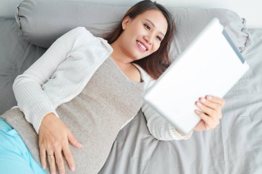 Mutlu genç güzel Vietnamlı kadın yatakta yatan ve dijital tablet komik videolar izlerken