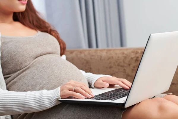 自宅のソファに座って インターネット上で妊娠に関する情報を検索する若い女性のトリミング画像 — ストック写真