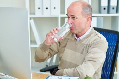 Bilgisayar ekranındaki bilgileri okurken sağlıklı orta yaşlı işadamı bir bardak tatlı su içiyor