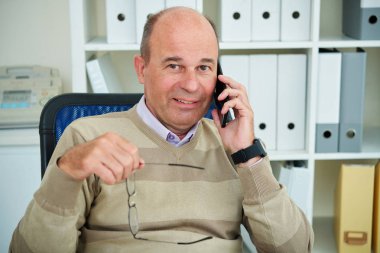Pozitif orta yaşlı adam gözlük lerini çıkarıp telefonla ararken kameraya bakıyor