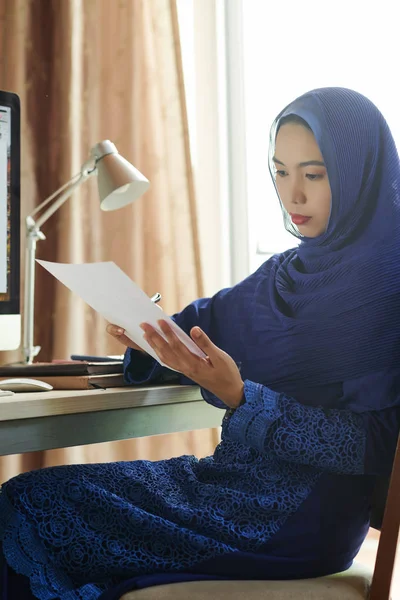 Alvorlig Tenkende Ung Muslim Forretningskvinne Som Sitter Ved Kontorbordet Leser – stockfoto
