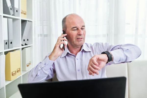 Geschäftsmann Mittleren Alters Sitzt Schreibtisch Und Checkt Beim Telefonieren Die — Stockfoto